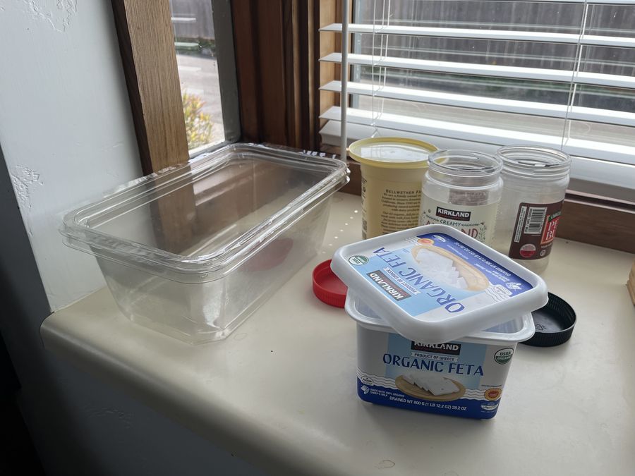 Empty Kirkland nut-butter jars, a feta tub and a yogurt cup, washed and set out on a windowsill.