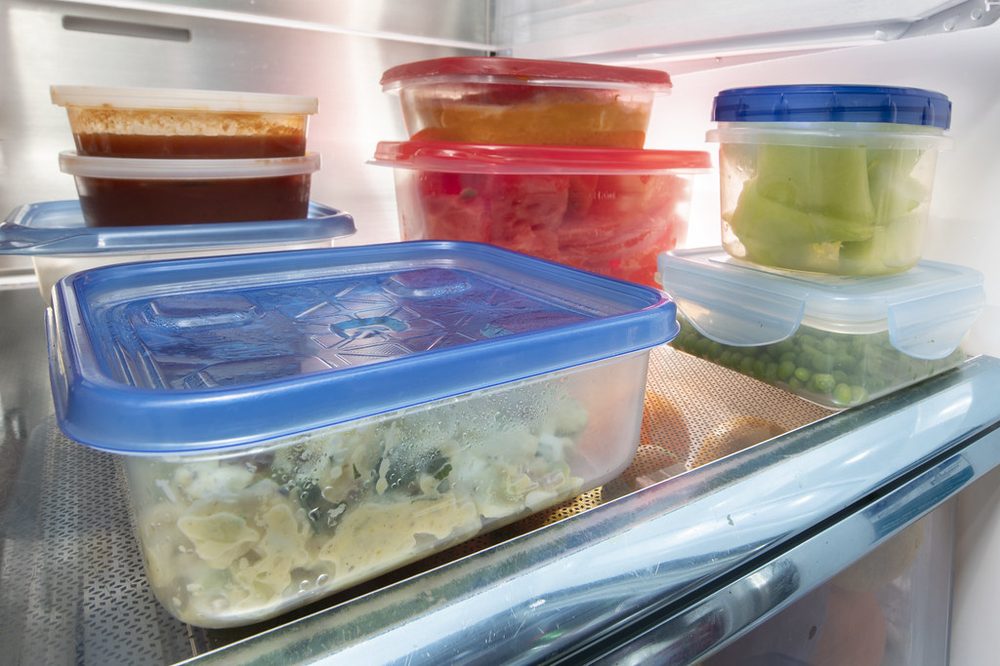 A refrigerator shelf of reused plastic tubs and containers, refilled with leftovers.